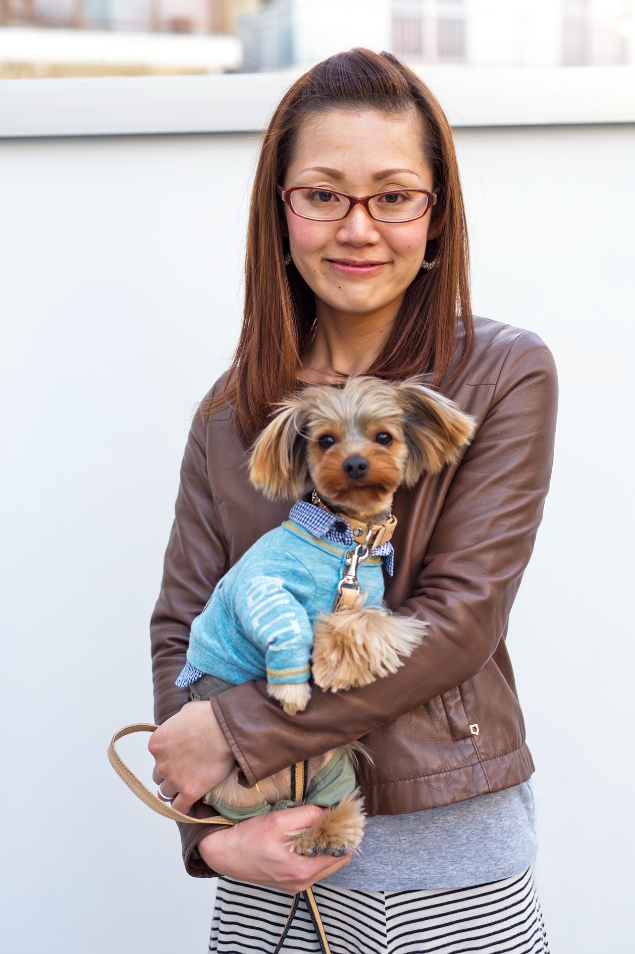 Woman holding a small dog wearing blue cargo pants and a checkered shirt.