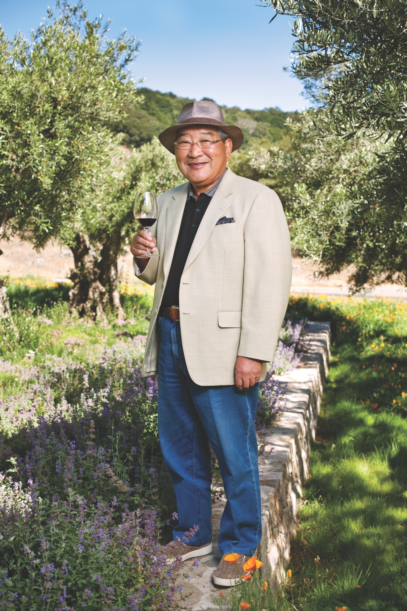 Kenzo Tsujimoto holding a glass of red wine standing in a vineyard at his Napa Valley estate.