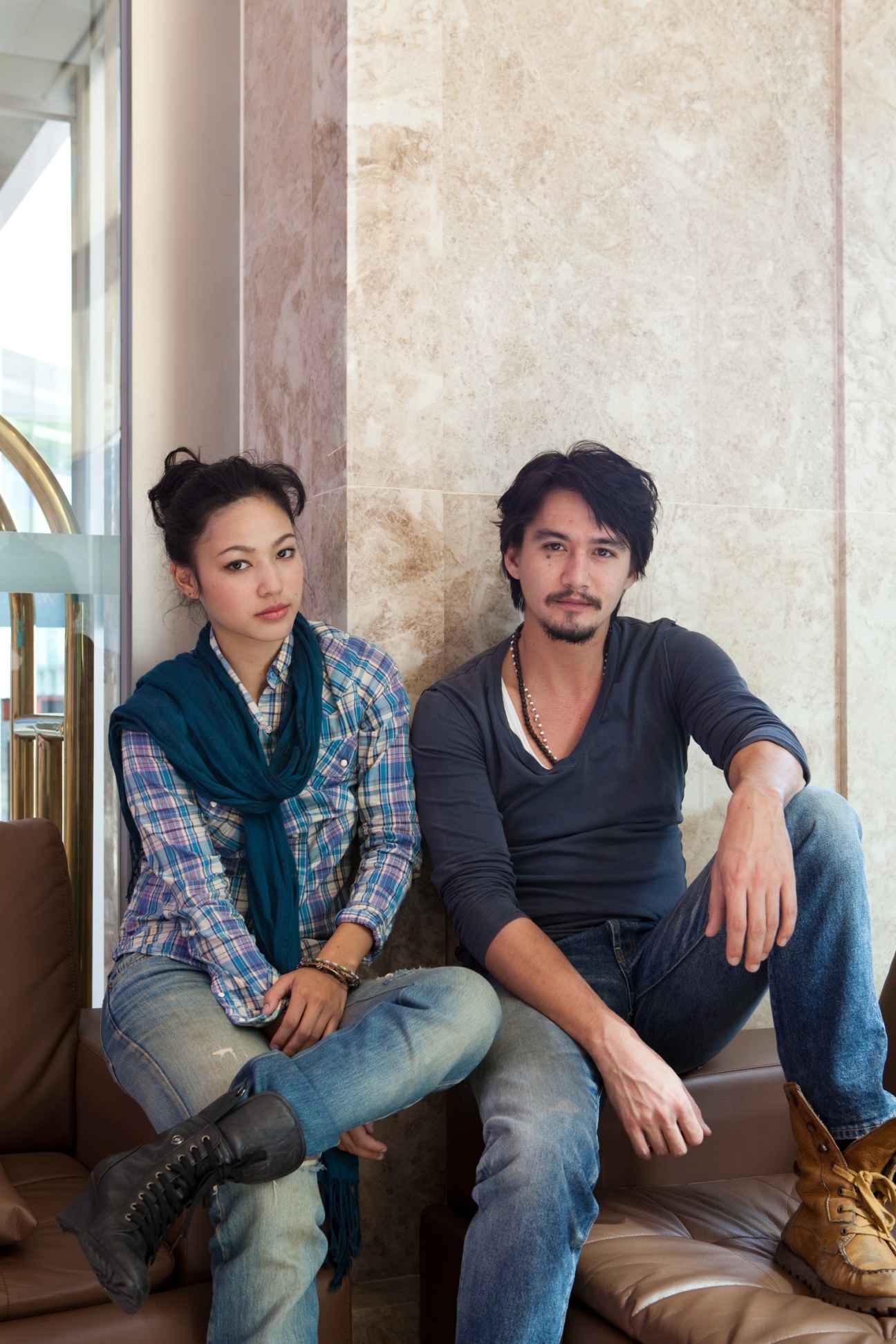 Thai actors Sajee Apiwong and Ananda Everingham sitting against a marble wall.