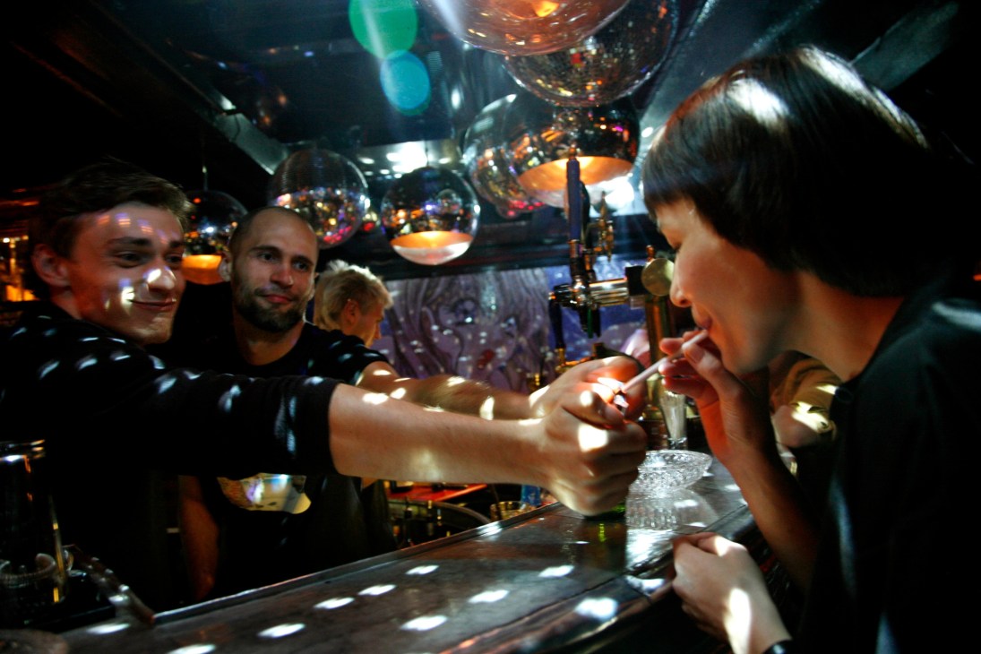 People socializing at a bar with ambient lighting and hanging lamps overhead.