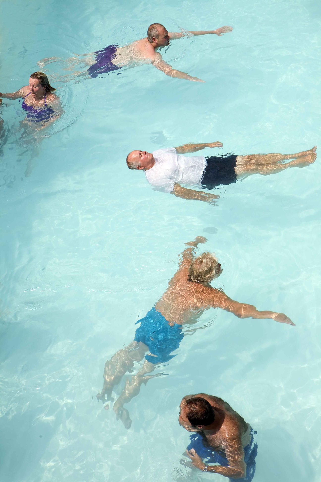 Five people floating and swimming in a bright turquoise pool.