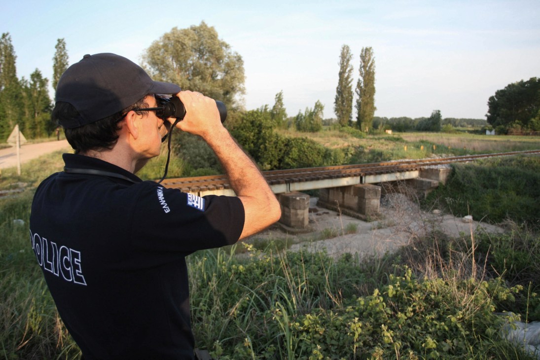 Police officer using binoculars at Greece-Turkey border to monitor illegal immigration crossings.