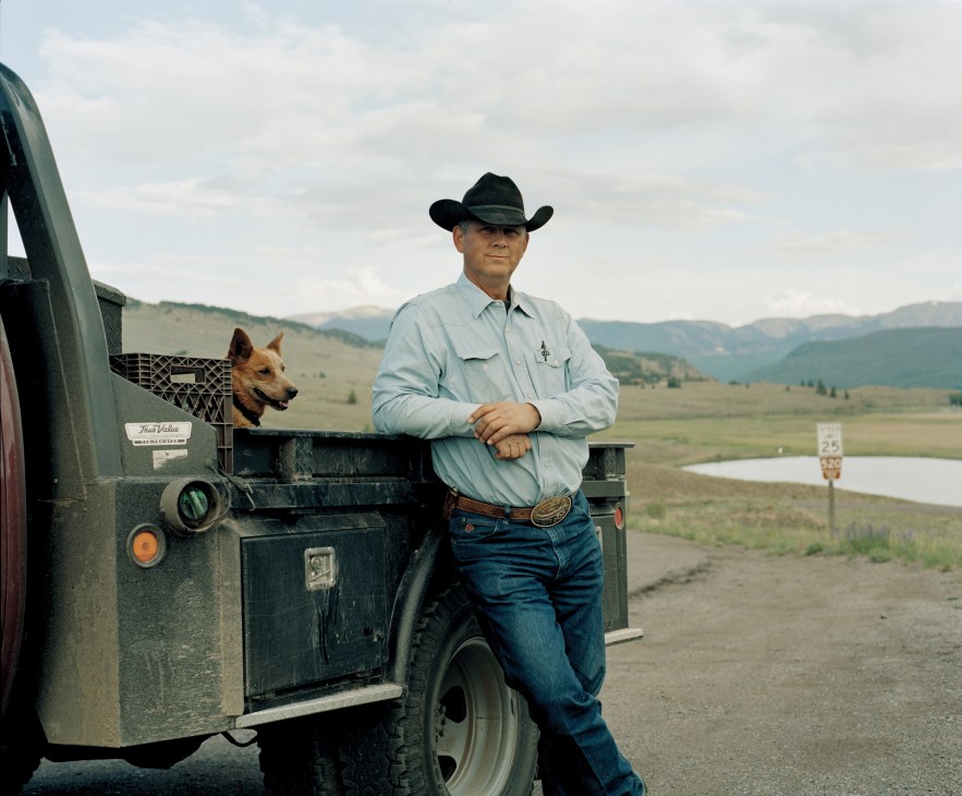 Cowboy Ted Harter stands beside a truck with his dog in Colorado mountains near the Rio Grande source.