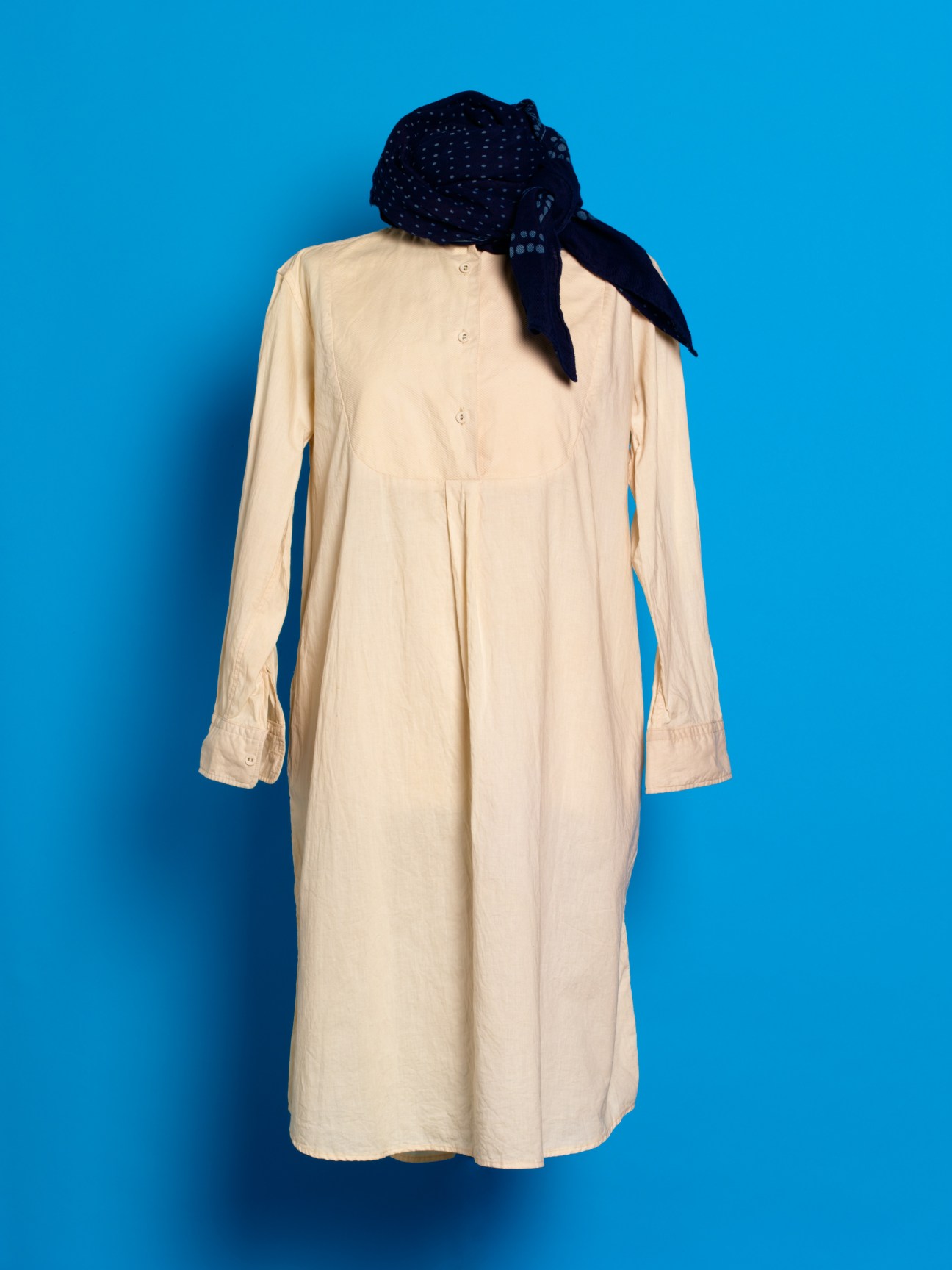 Cream cotton shirt-dress with navy blue headwrap against bright blue background.