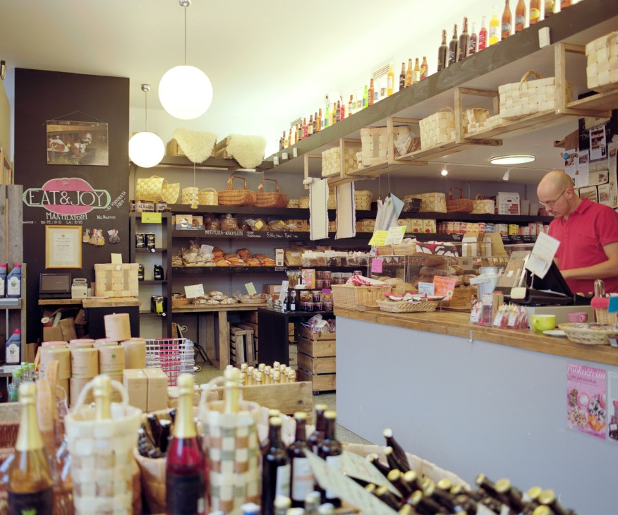 Interior of Eat & Joy Farmers Market showing shelves of packaged goods, bottles, and a man in a red shirt at the counter.