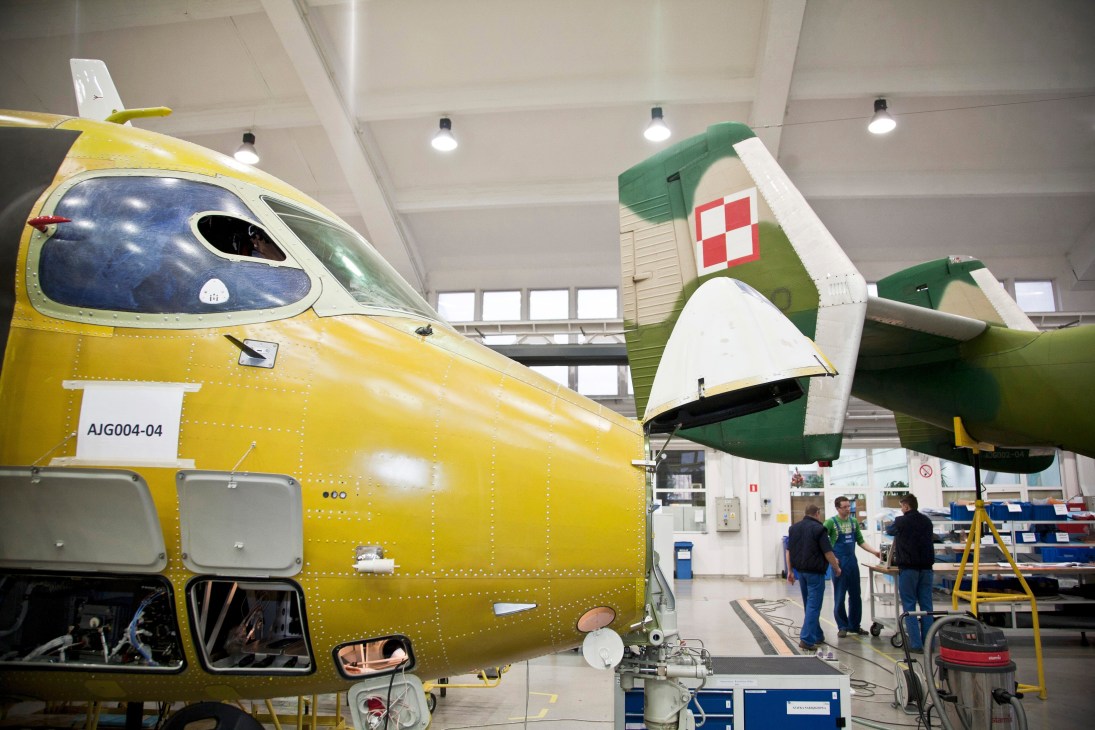 Yellow and green fixed-wing aircraft under construction in a bright hangar with workers nearby.