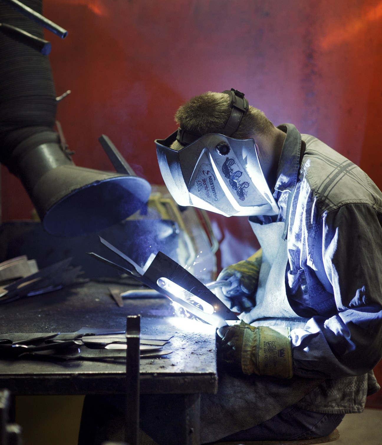 Worker in protective gear welding a tree spade at DeWit factory in bright blue arc light.