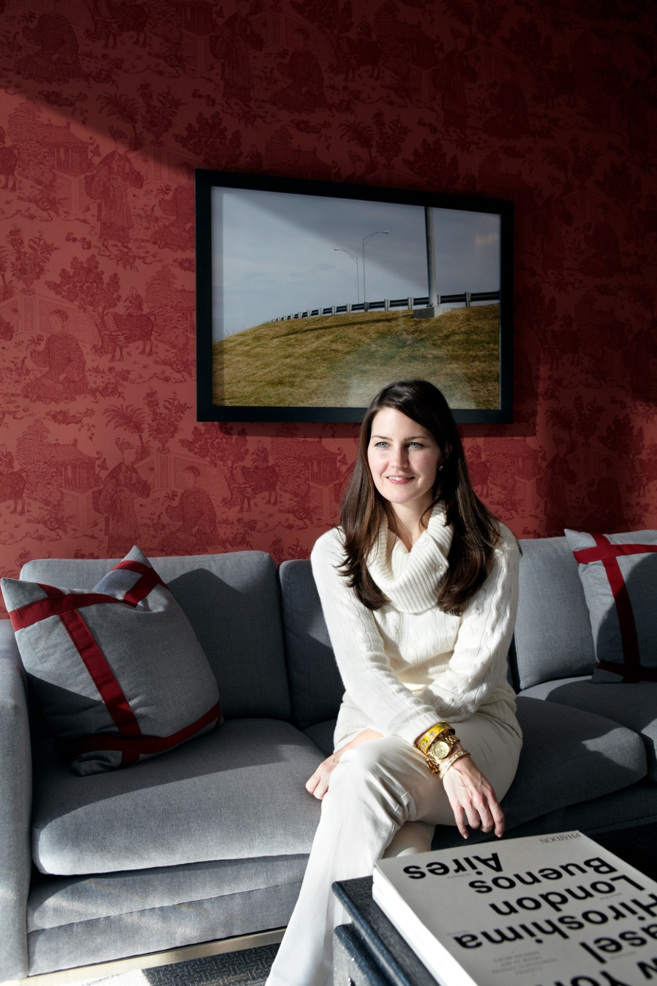 Megan Young sits on a gray sofa against a red patterned wall with a framed photograph above.