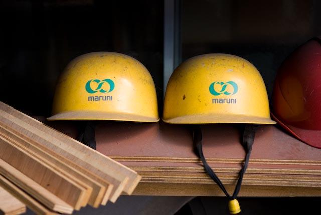 Two yellow hard hats with Maruni company logo displayed on a shelf in the factory.