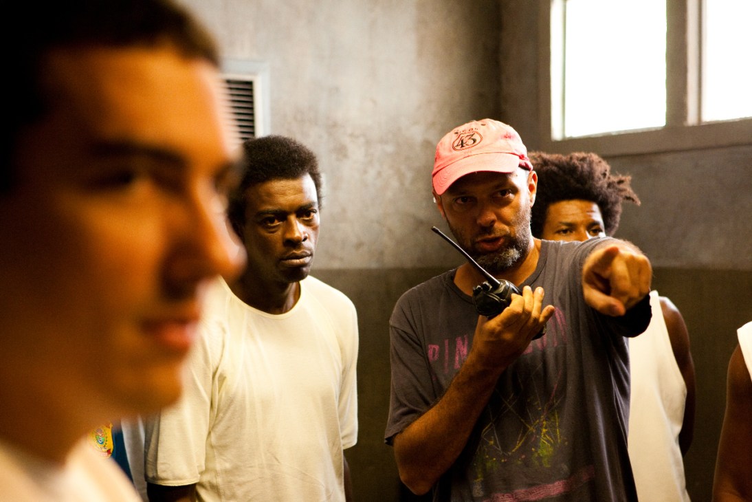 A director in a red cap gives instructions to actors on set during Elite Squad II filming.