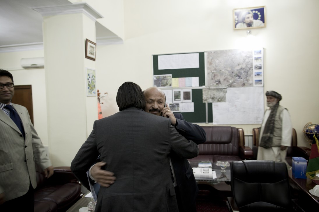 Mohammad Yunus Nawandish, Mayor of Kabul, embraces a visitor in his office with city planning documents on the wall behind them.