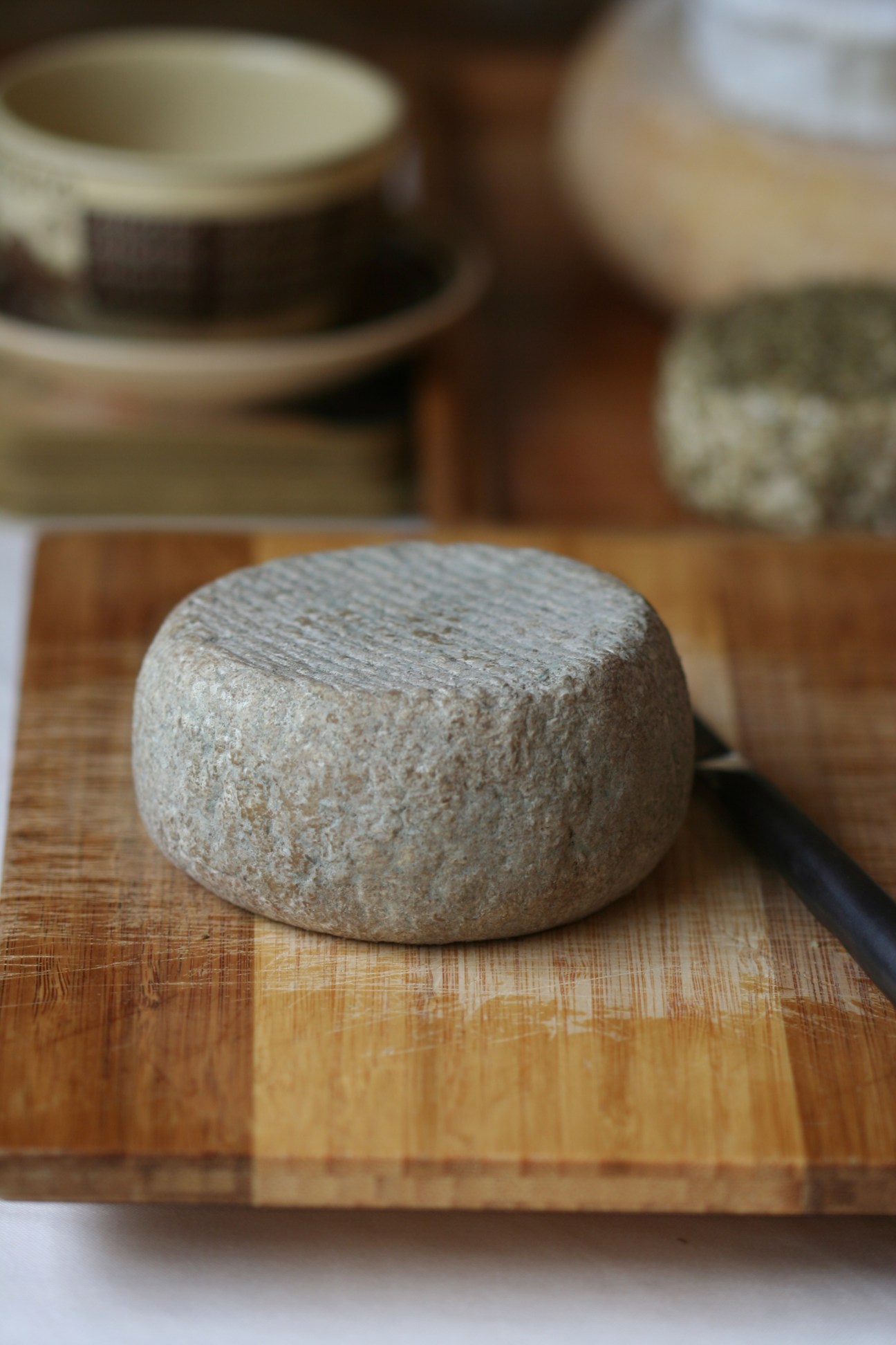 A round wheel of artisan cheese with a textured rind on a wooden cutting board.