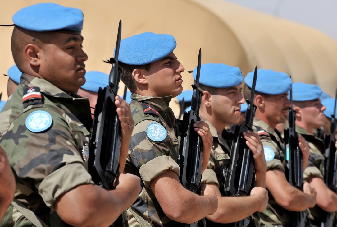 UN peacekeeping soldiers in blue berets and camouflage uniforms holding rifles in formation.