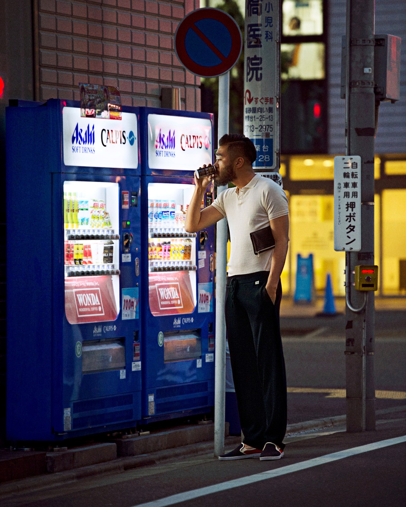 Man in white polo shirt standing by blue Asahi vending machine at night in Tokyo