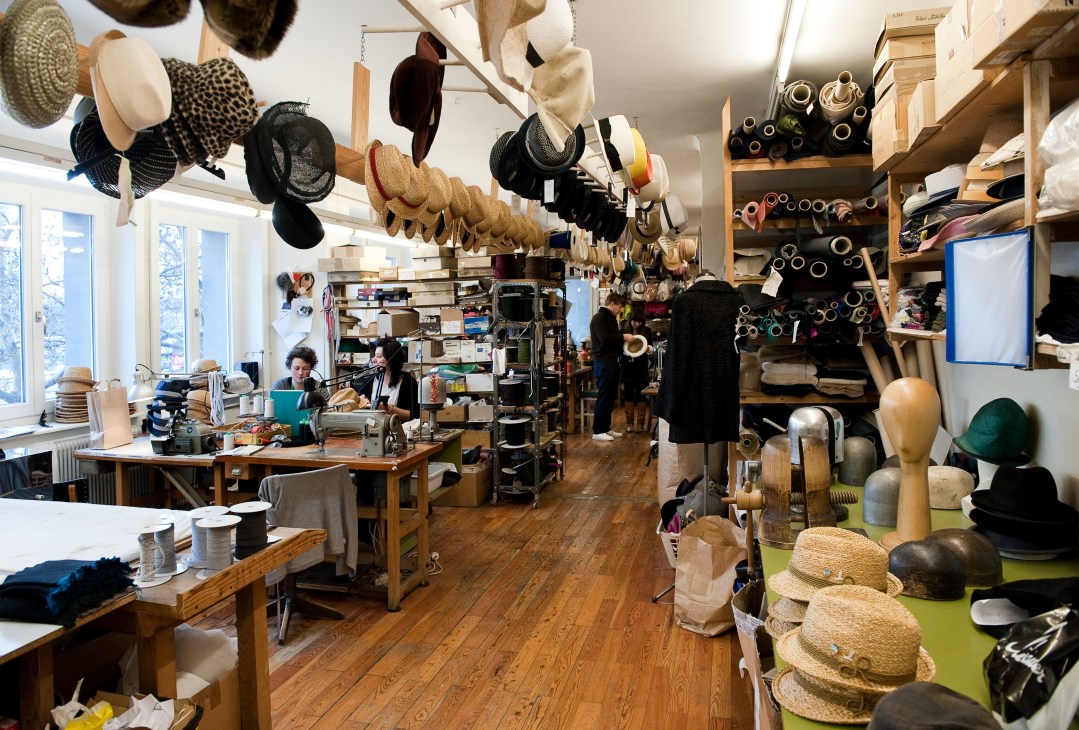 Interior of Mühlbauer hat workshop with finished hats hanging from ceiling and staff working at tables.