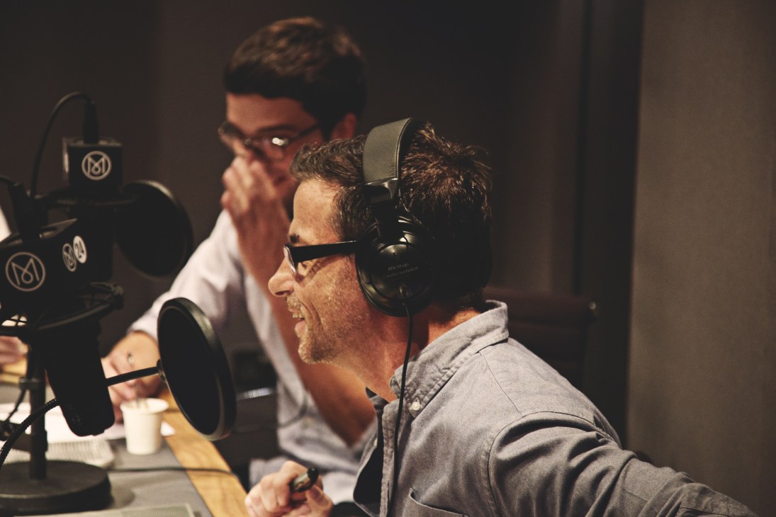 Editor Andrew Tuck wearing headphones at a microphone in Monocle 24 studio with Jonathan Openshaw visible in background.