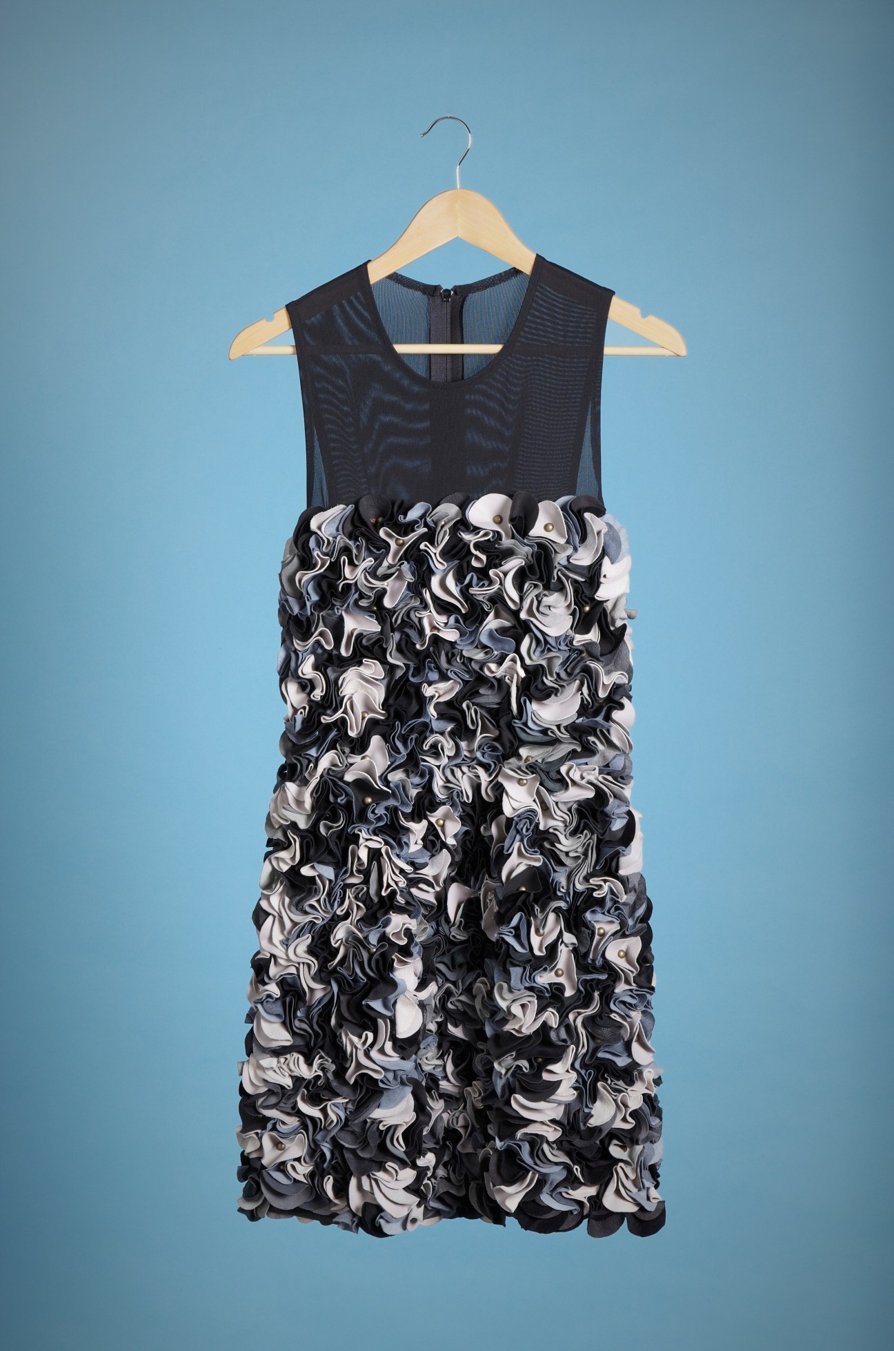 Black sleeveless dress with black and white textured ruffled skirt on wooden hanger against blue background.