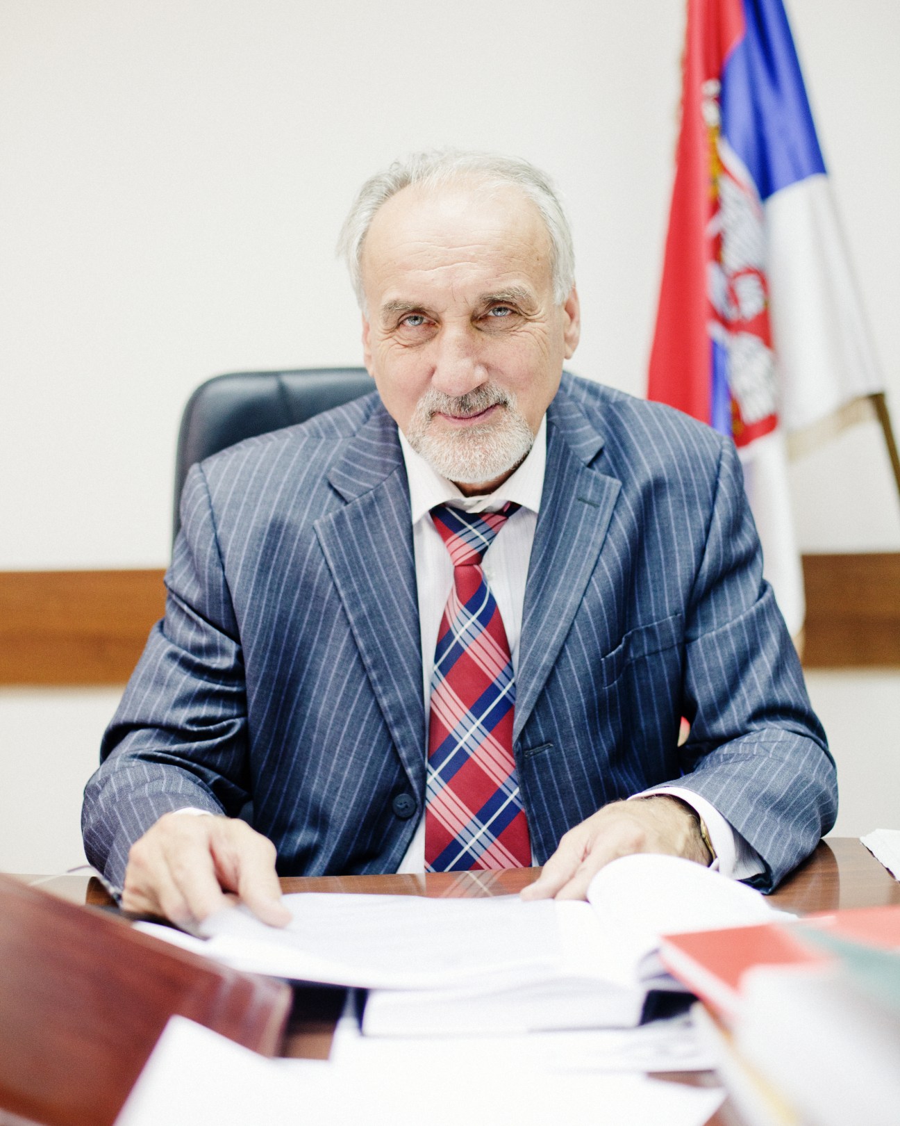 Vladimir Vukcevic, Serbian war crimes prosecutor, seated at desk with Serbian flag in background.