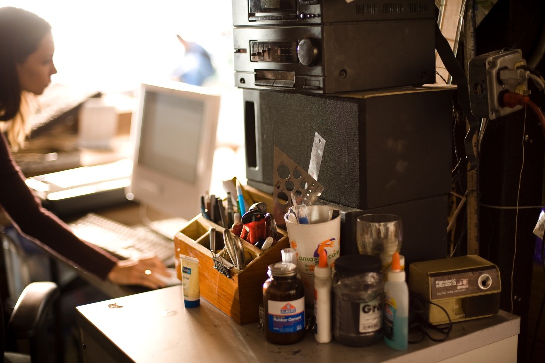 Artist Teresita Fernández working at her cluttered studio desk surrounded by tools and supplies.