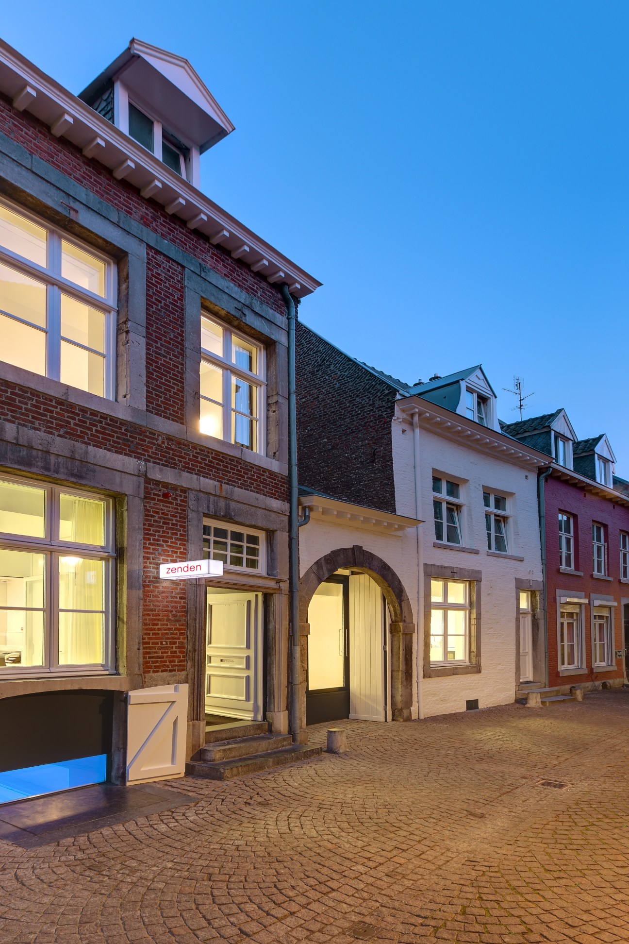 Hotel Zenden's exterior facade with illuminated windows at dusk, showing brick and stone architecture in Maastricht.