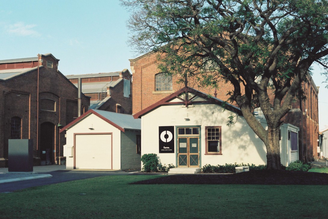 Form's office building The Nurses Post at Midland Atelier, a cream-colored cottage with red trim and wooden doors, surrounded by heritage red-brick buildings.