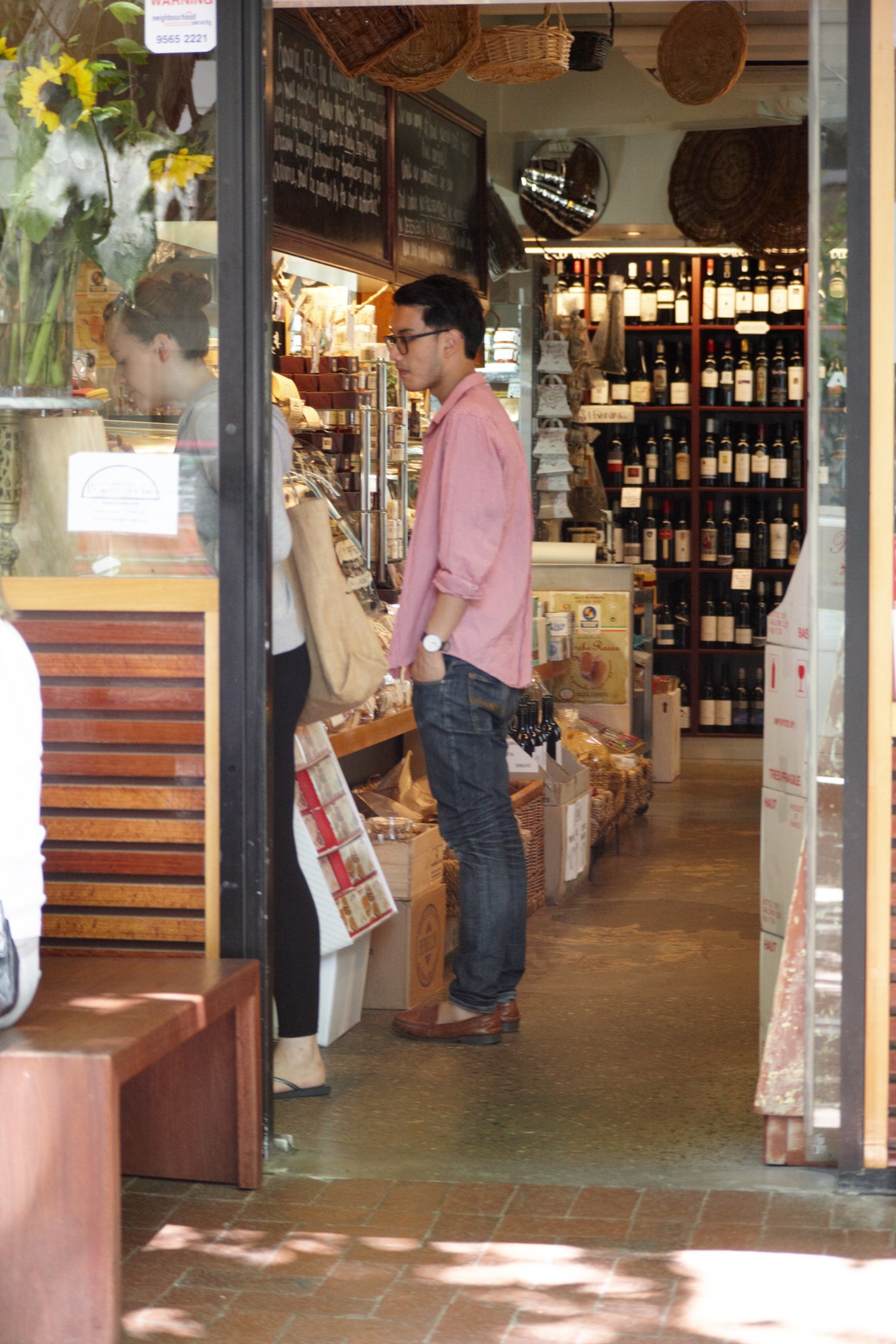 Customer browsing wine bottles inside Bottega del Vino, a wine shop in Potts Point with exposed brick and woven baskets.