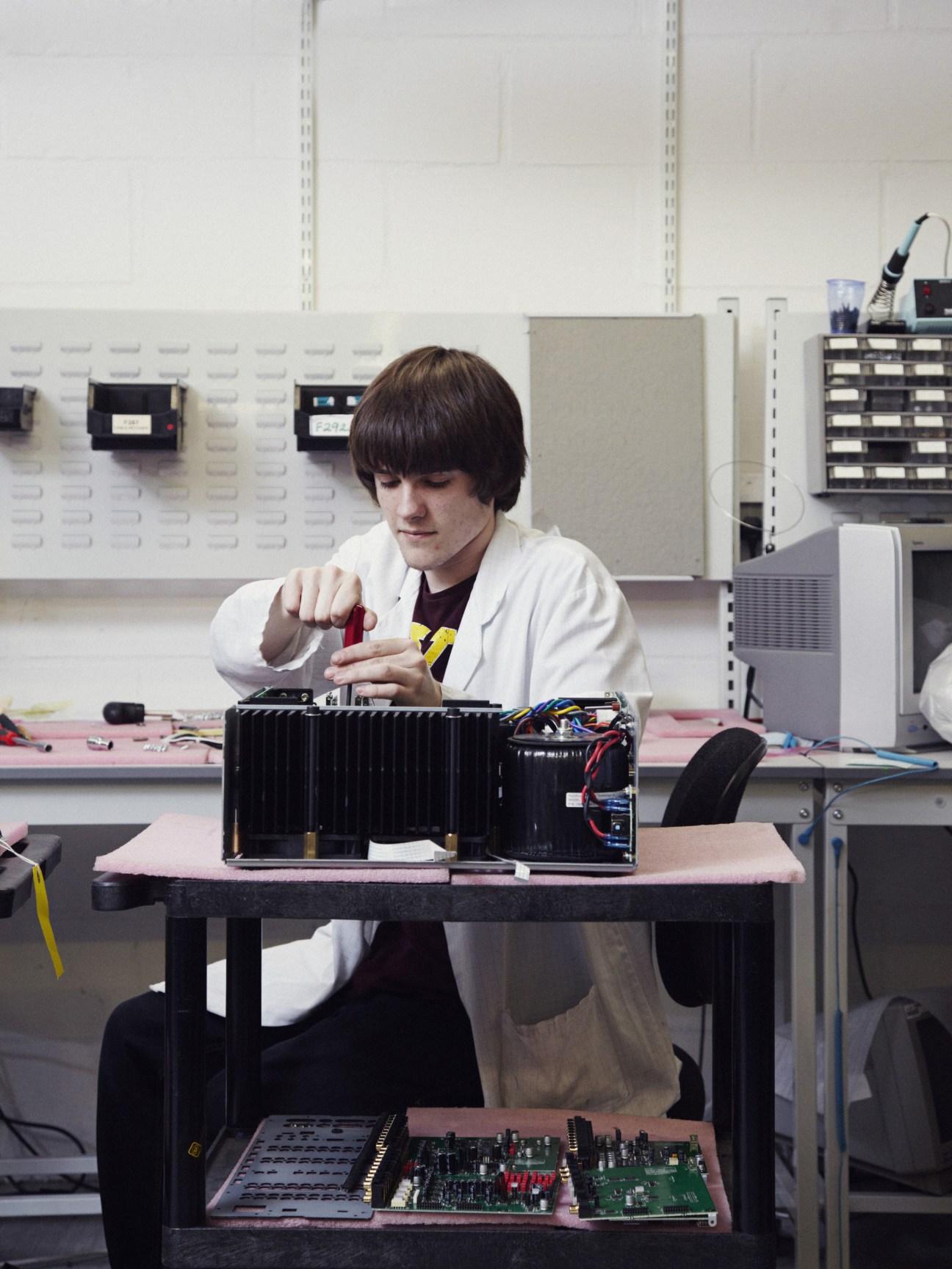 Technician in white coat assembles electronic circuits at workbench in Arcam factory.
