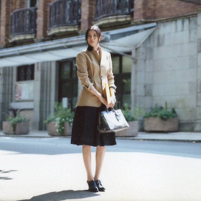 Woman wearing tailored jacket and skirt by Dries Van Noten with Prada bag on urban street.