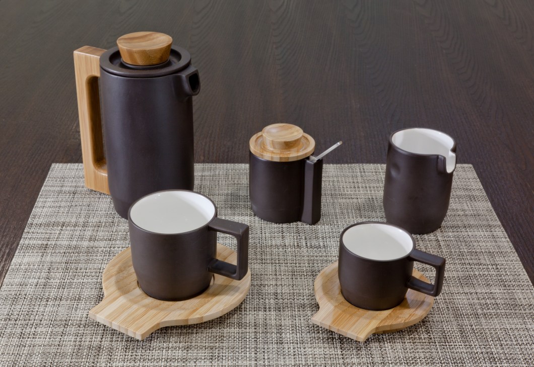 Purple clay coffee set by Jia with dark ceramic vessels, white interiors, and wooden handles and lids on a textured gray mat.
