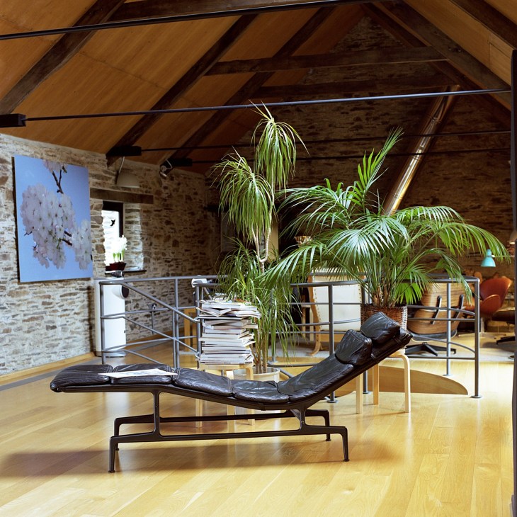 Interior of a converted farm building with exposed wooden beams, brick walls, modern furniture and a potted plant.
