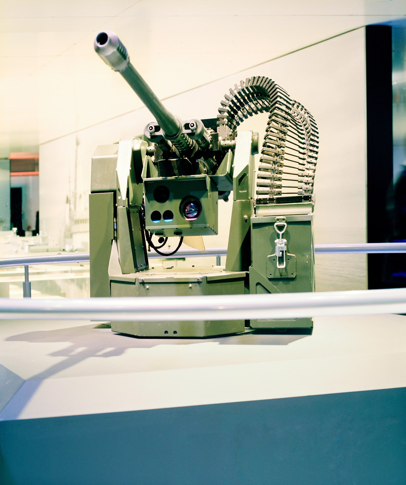 Remote weapon station with mounted cannon barrel and ammunition belt on display at arms fair.