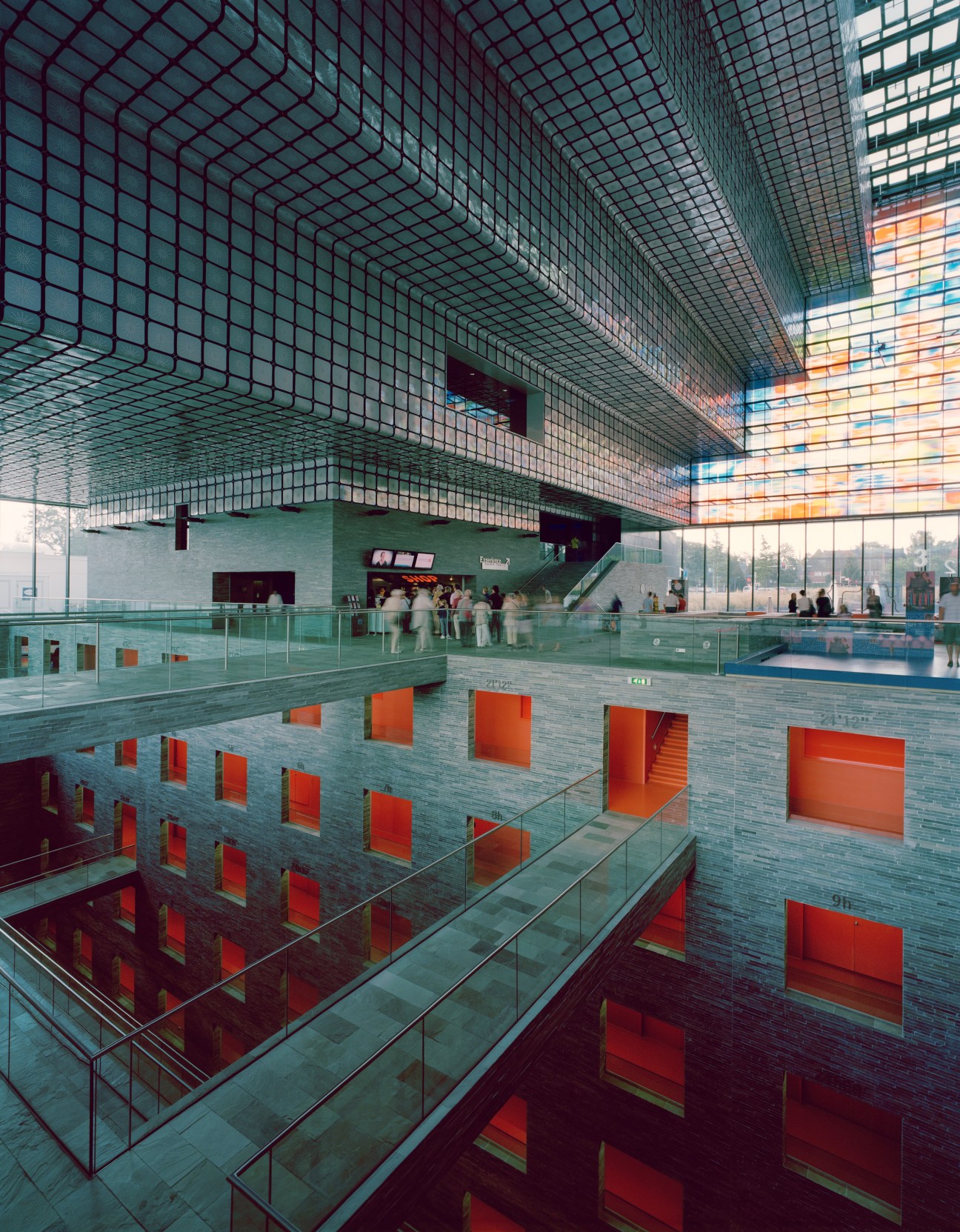 Half-subterranean atrium of the Netherlands Institute for Sound and Vision with grid ceiling, red window frames, and visitors.