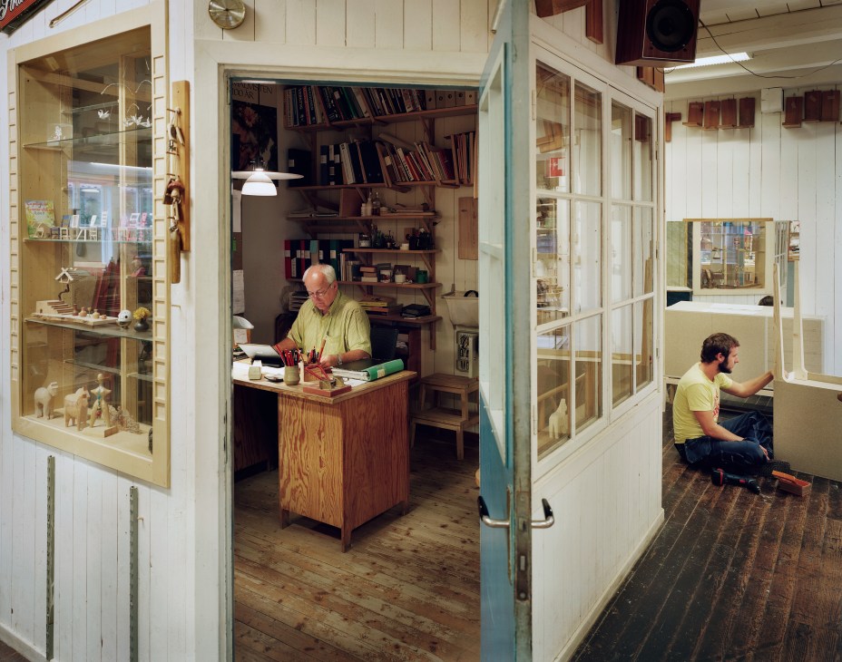 Woodworking studio with two craftsmen at work stations among shelves of wooden models and tools.