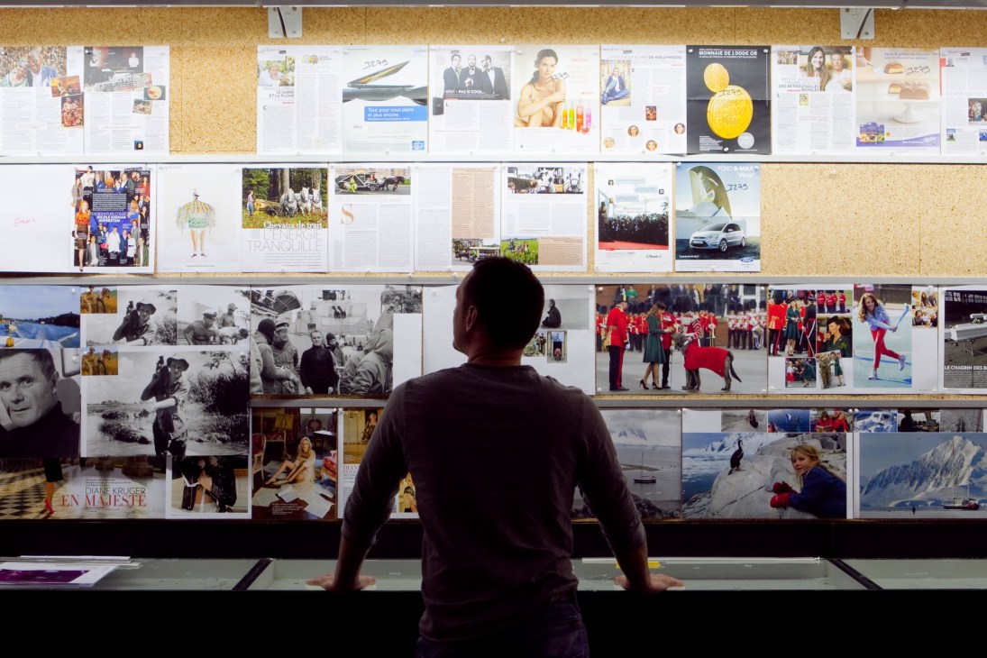 A person views Paris Match magazine covers and photographs displayed on a large wall.