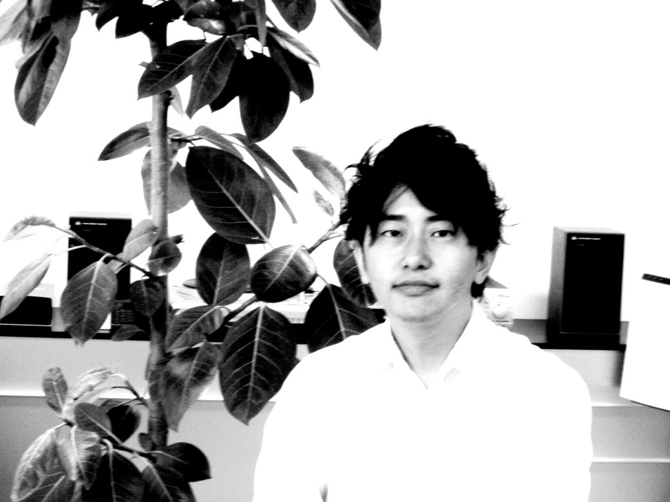 Portrait of Yoshinori Kobayashi, vinyl producer at Toyokasei, in black and white against a white background with plants.