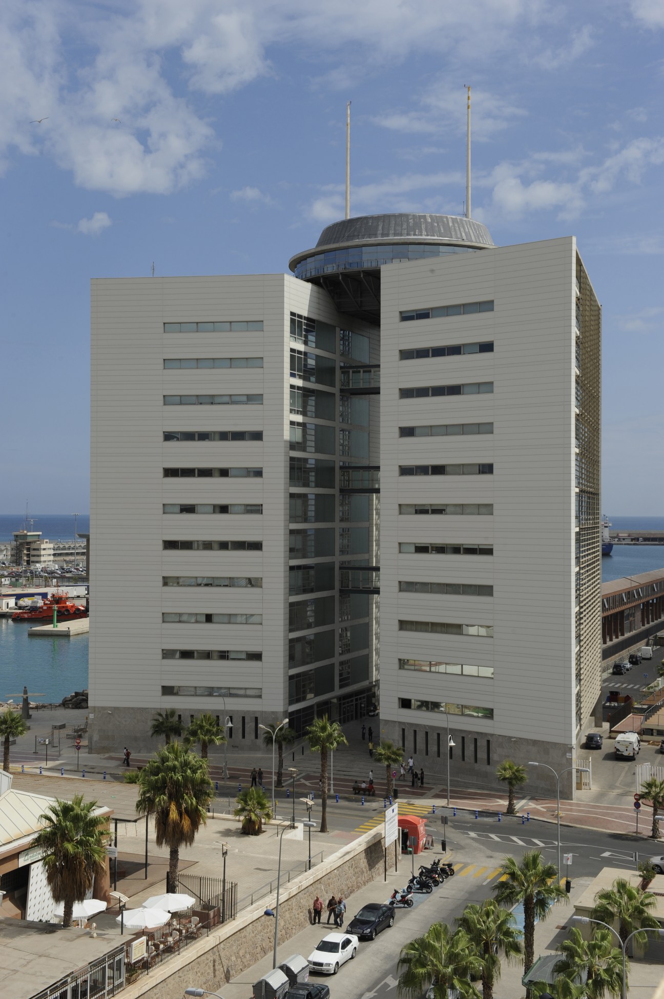 Modern white government delegation building with curved top structure and twin towers overlooking Melilla's port.