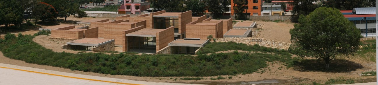 Aerial view of Oaxaca School of Fine Arts showing rammed earth and concrete modular buildings nestled in arid landscape.