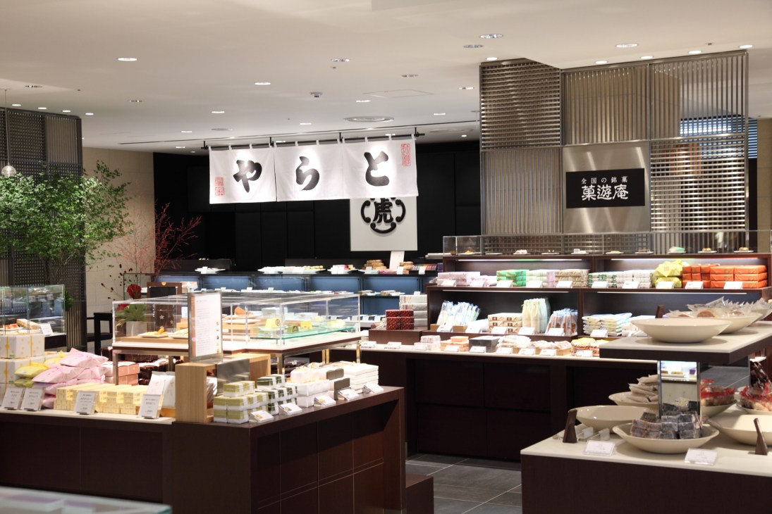 Interior of Mitsukoshi's food hall showing display cases with Japanese confectionery and products arranged across dark counters with illuminated signage.