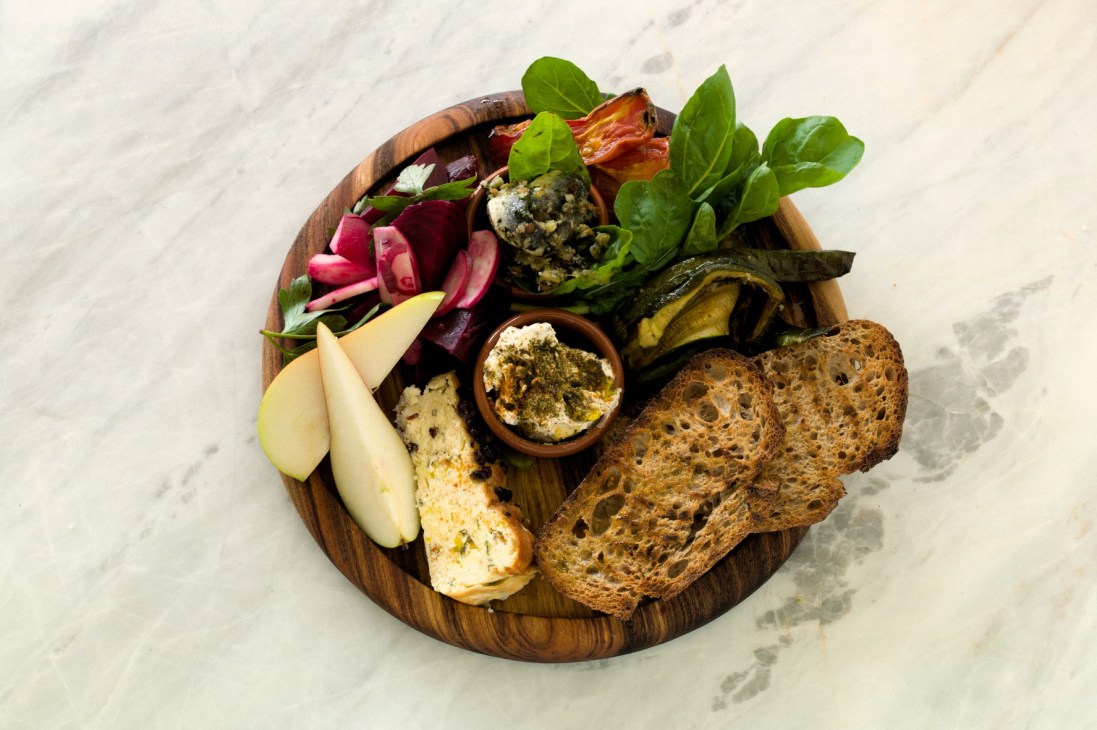 Wooden plate of artisanal food including cheese, bread, vegetables and spreads at Cornersmith cafe.
