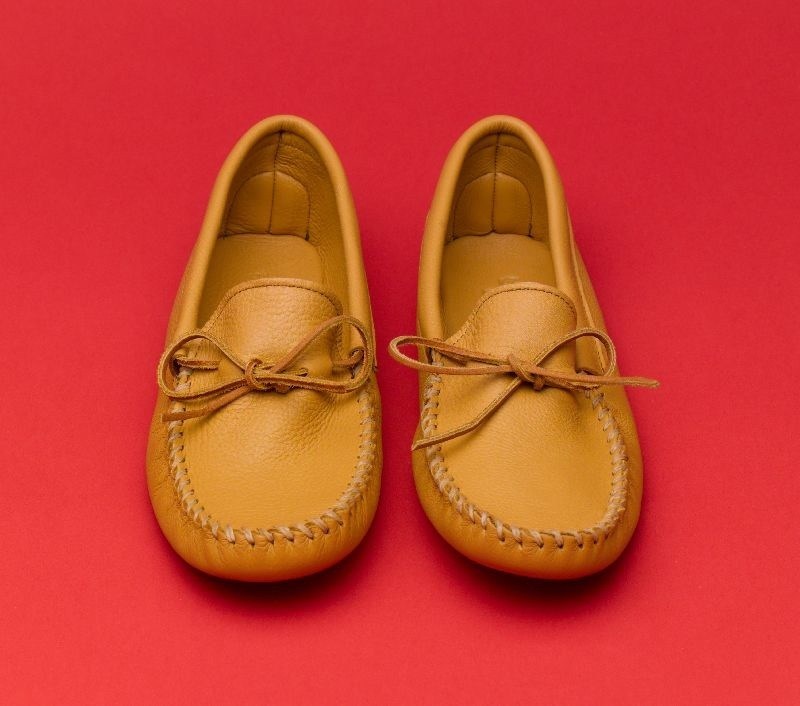 Pair of mustard-colored deerskin driving shoes by Minnetonka on a red background.