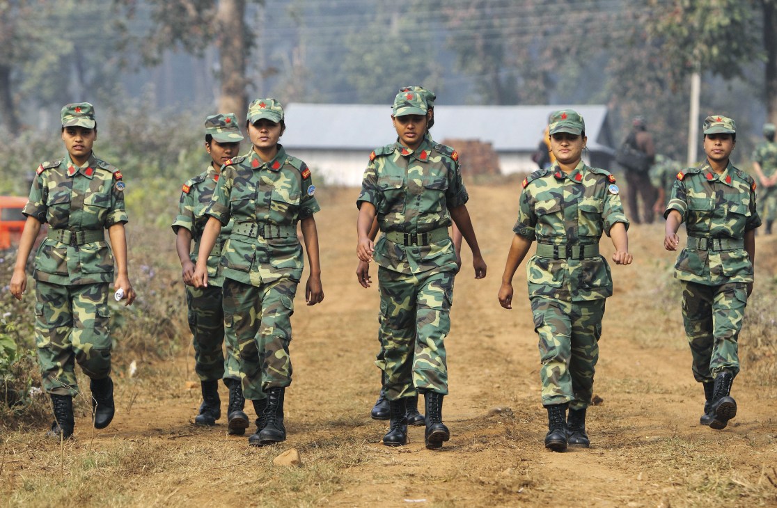 Six military personnel in camouflage uniforms walking on a dirt road.
