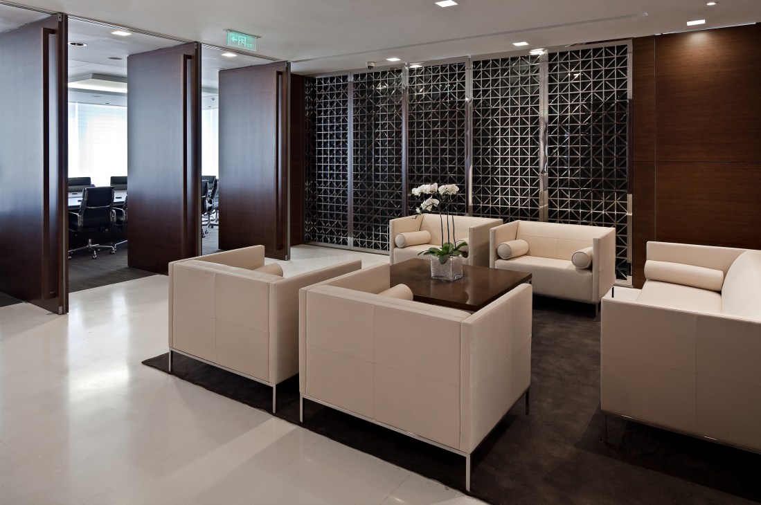 Modern office lounge with cream-colored seating, dark wood paneling, and geometric patterned screens at HSBC Shanghai headquarters.