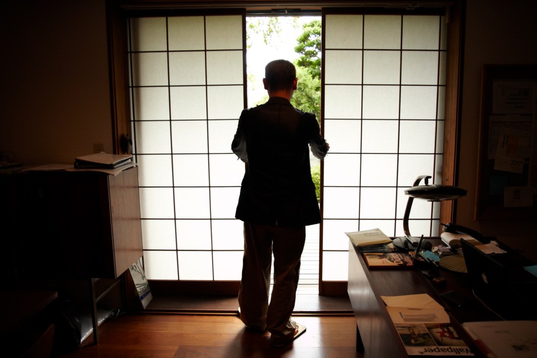 Man in dark suit standing at shoji screen doors overlooking a garden at Simplicity HQ in Tokyo.