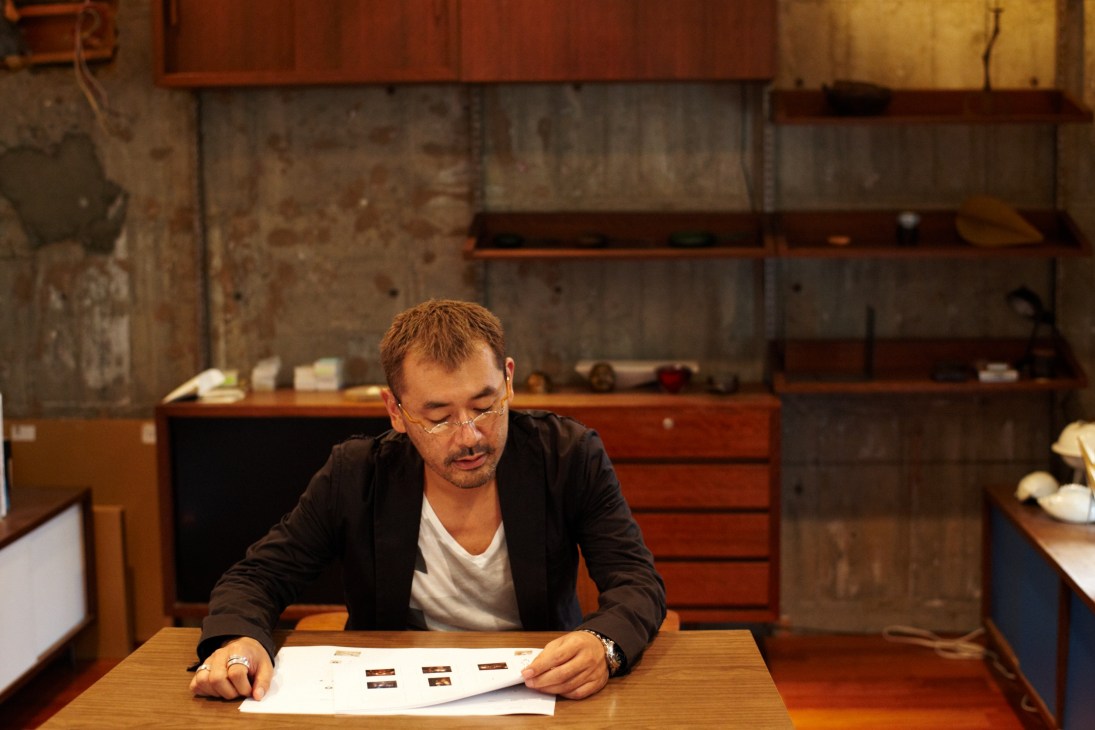 Man in black blazer reviewing design materials at wooden desk in modern office space.