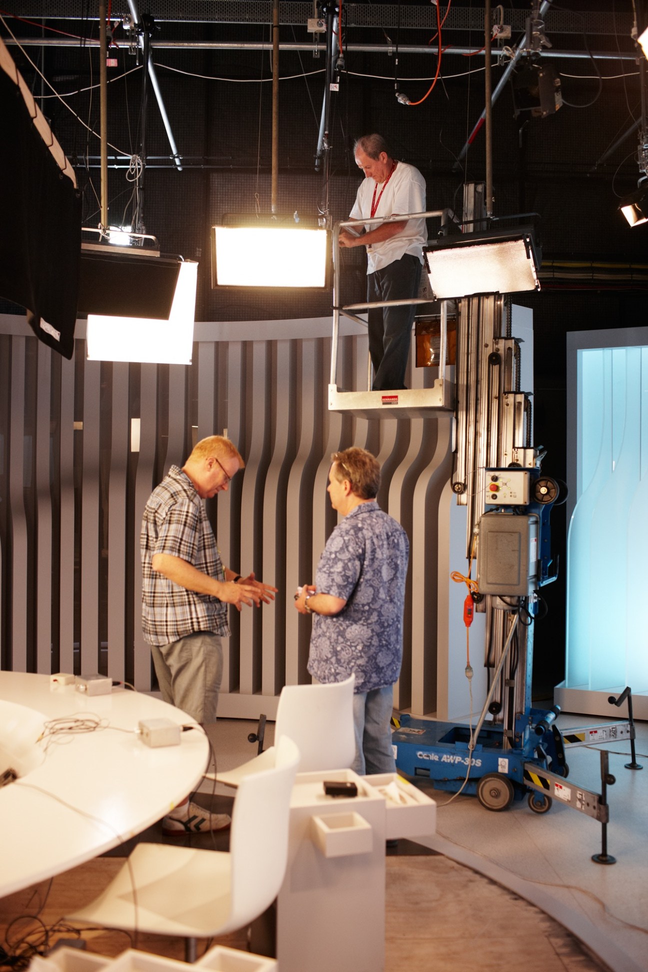TV studio technicians working in a professional broadcasting studio with lighting equipment and striped backdrop walls.