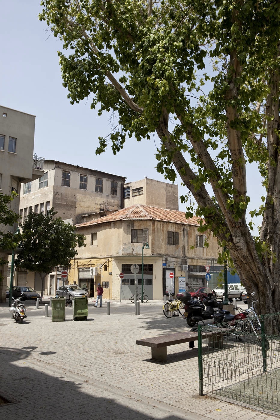 Sgula Square in Noga with historic Mediterranean architecture, tree-lined plaza, and local residents.