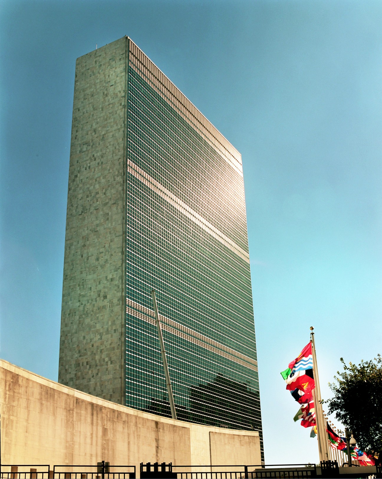 The UN Headquarters building in New York with international flags in front under clear blue sky.