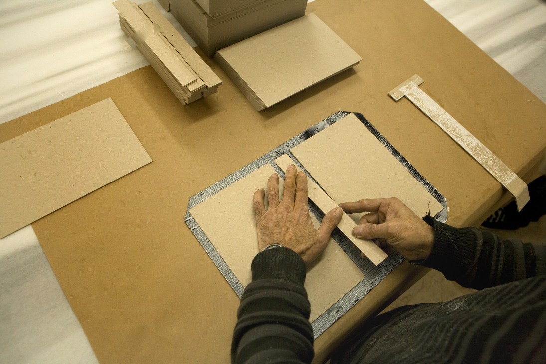 Hands working on binding an Ece diary with cotton backing and decorative trim during handmade production.
