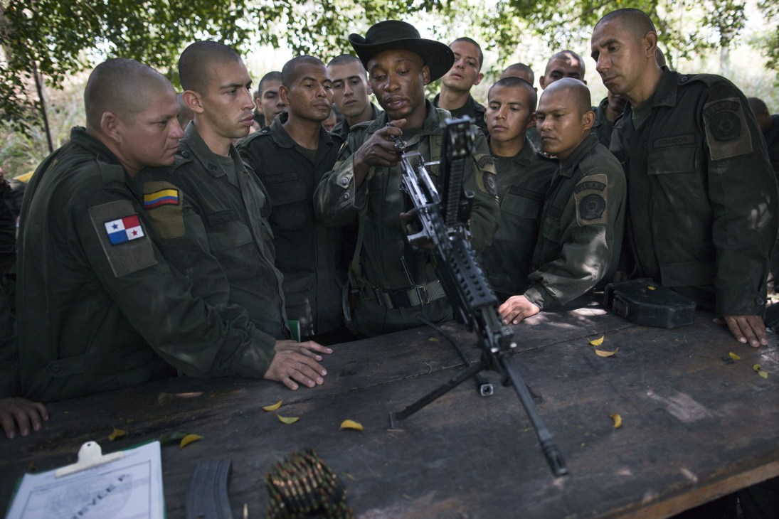 Latin American police and military students gathered around a table learning to disassemble a rifle during training.