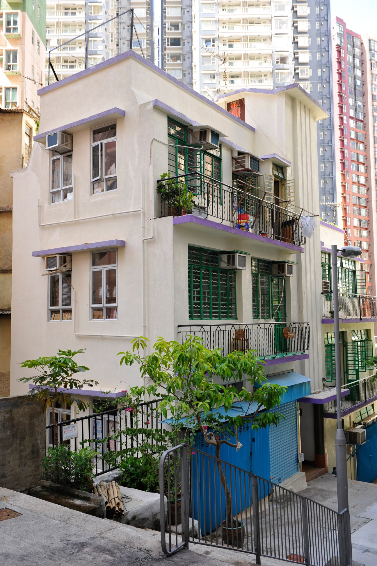 A colorful traditional building with purple trim and green shutters surrounded by modern high-rises in Hong Kong's Sheung Wan district.